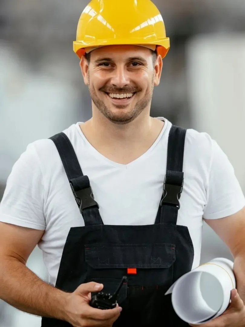 hochkantige Ansicht eines Elektrotechniker lächelt in die Kamera und hält in seiner Hand einen Installationsplan