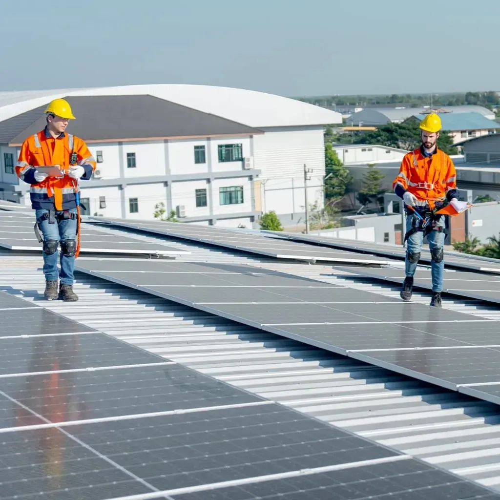 2 Elektrotechniker kontrollieren die Photovoltaikanlage auf dem Dach einer Produktionshalle