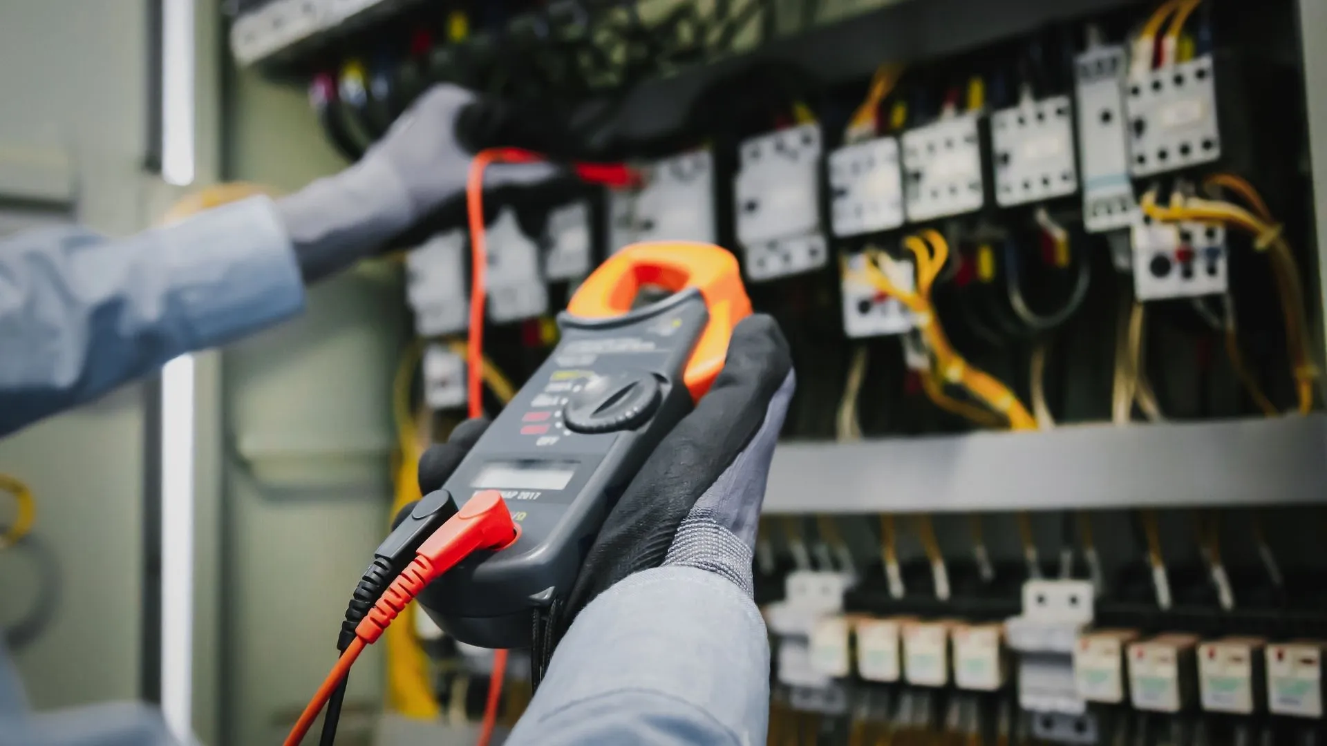 Elektriker richtet Messinstrumente ein um damit den Schaltschrank im Hintergrund zu überprüfen