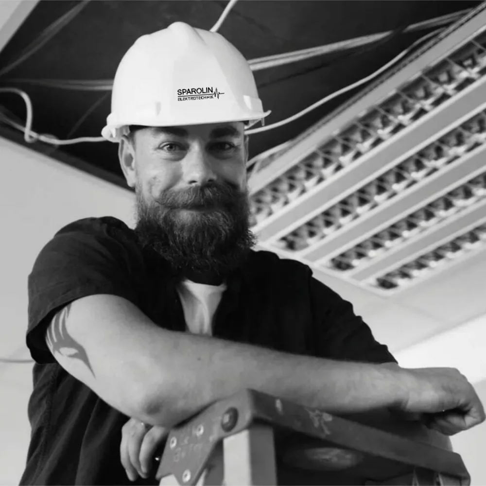 Ein lächelnder Elektriker mit Vollbart und Tattoo