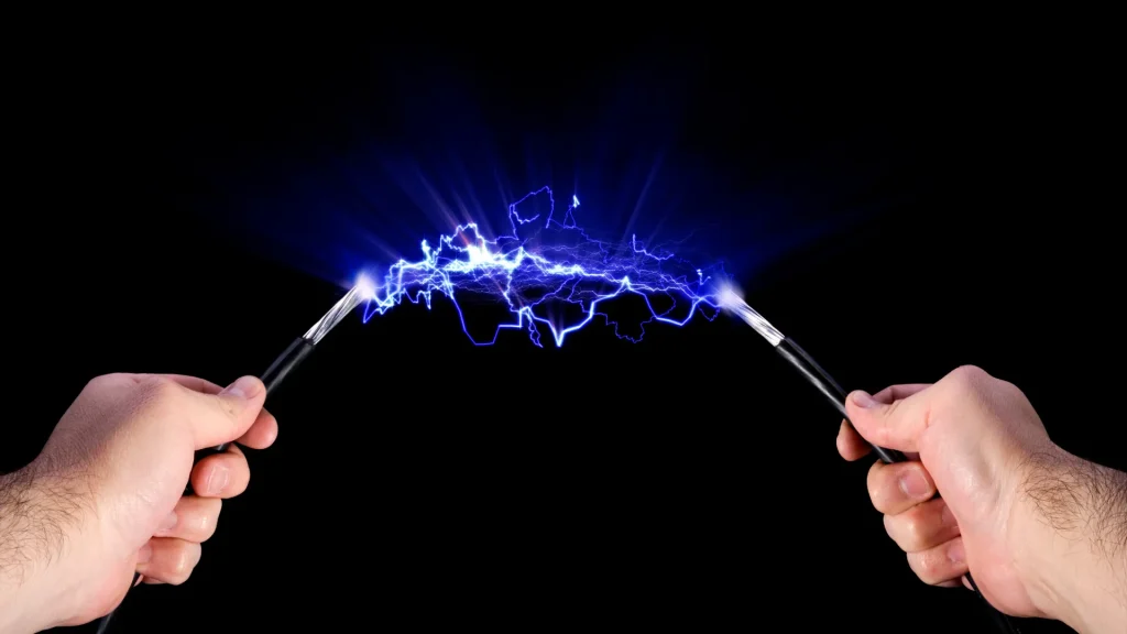 2 Hände halten jeweils das Ende eines Kabels. Zwischen den Enden hat isch ein Lichtbogen aufgebaut